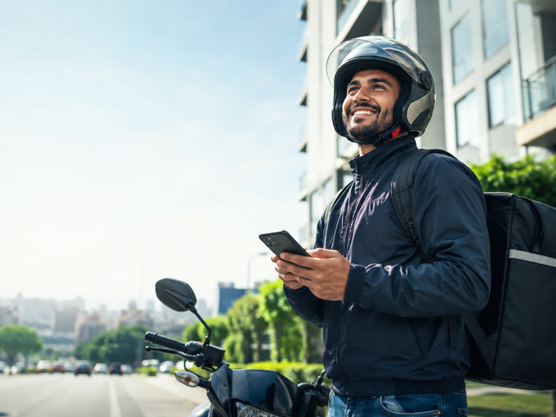 Motorista de aplicativo consultando o celular ao lado da moto